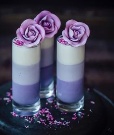 two glasses filled with purple flowers on top of a black plate and sprinkles