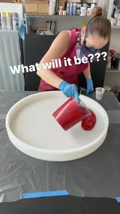 a woman in red shirt and blue gloves cutting up a plastic object on top of a table