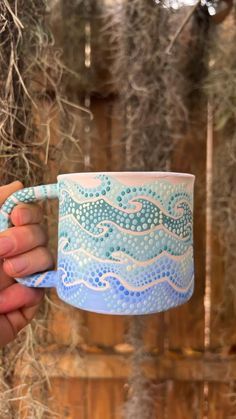 a hand holding a blue and white coffee mug in front of a wooden wall with plants