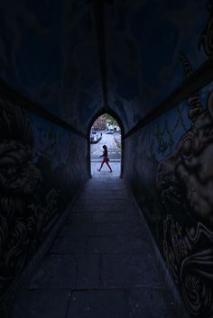 a person walking down a dark tunnel with graffiti on the walls