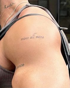 the back of a man's shoulder with tattoos on it and words written in cursive writing