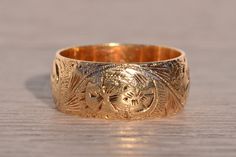 The Chartres: Antique Hand Engraved Band in Yellow Gold. Exuding timeless elegance, this antique yellow gold band boasts a generous width of 8.9mm, adorned with intricate hand-engraved scrolled and floral patterns. Crafted with meticulous attention to detail, the band showcases the artistry of its 14 karat yellow gold composition. Currently sized at 9.75, it can be delicately adjusted to achieve a perfect fit for an additional charge upon request. Love this piece, but don't have the money to spe Luxury Etched Heirloom Bands, Luxury Yellow Gold Engraved Ring In Recycled Material, Luxury Antique Gold Bracelet Engraved, Traditional Etched Yellow Gold Engraved Ring, Traditional Yellow Gold Engraved Ring, Traditional Gold Engraved Ring With Decorative Band, Traditional Engraved Yellow Gold Ring, Heirloom Yellow Gold Carved Engraved Ring, Traditional Carved Engraved Wedding Ring