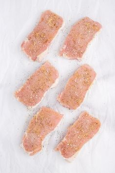 four pieces of raw meat sitting on top of a piece of parchment paper with seasoning sprinkles