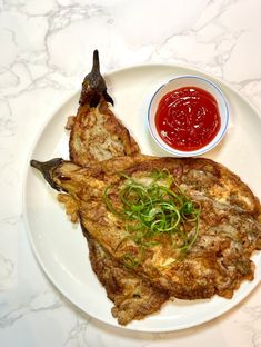 a white plate topped with fried fish next to a bowl of ketchup and sauce