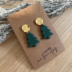 the green and gold christmas tree earrings are sitting on top of a brown cardboard card