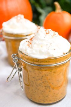 two jars filled with whipped cream sitting on top of a table next to pumpkins