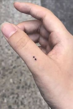 a tiny black dot tattoo on the middle finger