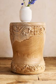 a vase with flowers in it sitting on a wooden table next to a white wall