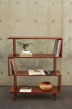 a wooden shelf with books, magazines and a potted plant sitting on top of it