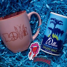 a pink coffee mug next to a sticker and blue shredded paper with the words, wildness cajun salt on it