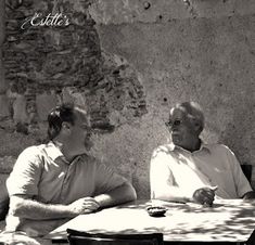 two older men sitting at a table outside