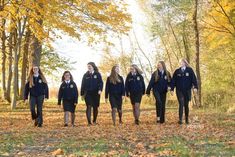 a group of girls in school uniforms are walking through the woods with leaves on the ground