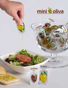 a person pouring olives into a salad in a glass bowl with bread on the side