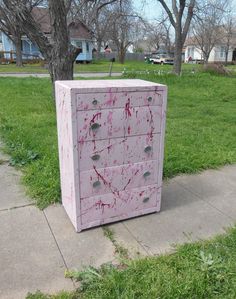 a pink dresser sitting on top of a sidewalk next to a green grass covered field