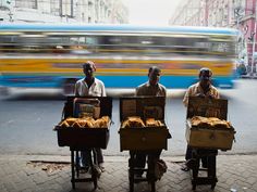 three men are selling bread on the side of the road in front of a bus