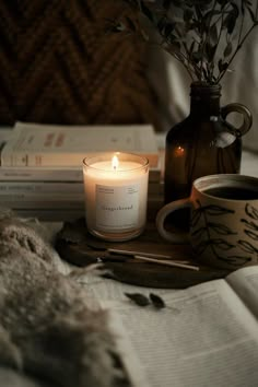 a candle and some books sitting on a bed next to a vase filled with flowers