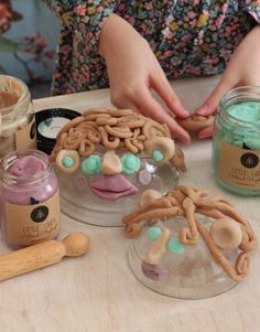 a person making cookies on a table with jars and spoons next to the doughnuts