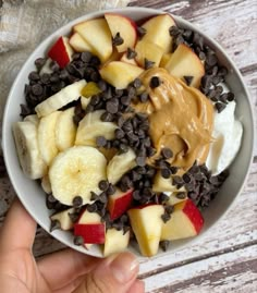 a bowl filled with fruit and chocolate chips on top of a wooden table next to a person's hand