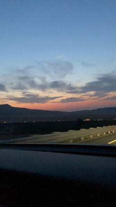 the sun is setting over some mountains in the distance as seen from a moving car