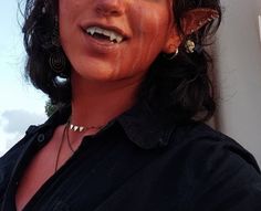 a close up of a person wearing earrings and a black shirt with blue sky in the background