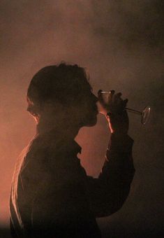 the silhouette of a man drinking from a wine glass in front of a dark background