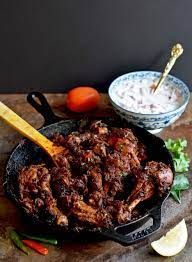 a skillet filled with meat and vegetables on top of a wooden cutting board next to a bowl of rice