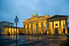 a large building with columns lit up in the evening time at dusk or dawn, and people walking around it