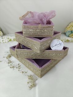 three decorative boxes are stacked on top of each other, one with a purple bow