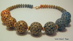 three different colored beads on a necklace with gold and silver accents, sitting on a white surface