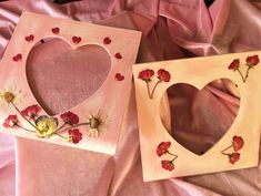 two wooden frames decorated with flowers and hearts on pink satin fabric, one is shaped like a heart