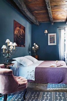 a bedroom with blue walls, purple bedding and two chairs in front of the bed