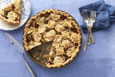 a pie sitting on top of a blue table cloth next to a knife and fork