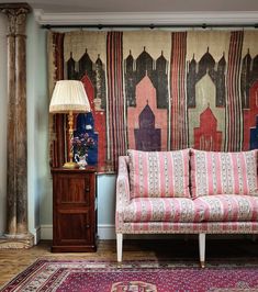 a pink couch sitting on top of a wooden floor next to a lamp and rug