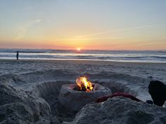 there is a fire pit on the beach with people in the background and one person standing at the water's edge