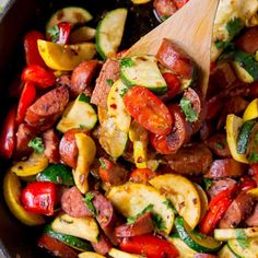 a skillet filled with sausage, peppers and zucchini on top of a wooden spoon