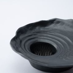 a black ceramic bowl sitting on top of a white table next to a cup brush