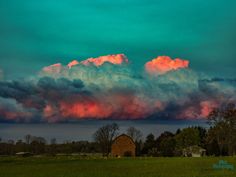 the sky is filled with pink clouds as it sits in front of a green field