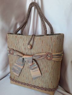 This particular bag is made with upholstery fabric on an eco-leather base. The point of union between the leather and the fabric is hidden by a series of small rings, covered with cotton thread. Four larger loops, lined with the same cotton, hold a silk ribbon that surrounds the bag and is tied with a ribbon at the front of the bag. The handles are made with a cord covered in crocheted chenille; their length allows the bag to be worn by hand or on the shoulder. The closure is formed by a button Brown Fabric Tote Shoulder Bag, Brown Fabric Tote Bag, Fabric Shoulder Bag With Adjustable Strap For Shopping, Beige Fabric Shoulder Bag With Adjustable Strap, Elegant Shoulder Bag With Loop Closure For Daily Use, Elegant Brown Woven Shoulder Bag, Elegant Woven Square Shoulder Bag, Elegant Square Woven Shoulder Bag, Brown Fabric Rectangular Shoulder Bag