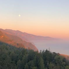 the sun is setting over some mountains with trees and fog in the foreground, as seen from an overlook point