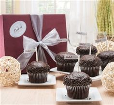 chocolate cupcakes are sitting on small plates in front of a red gift box