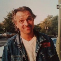 a man wearing a jean jacket standing next to a parking meter