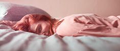 a woman laying in bed with pink sheets