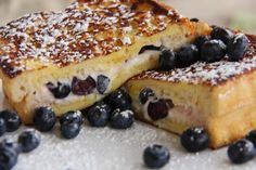 two pieces of french toast with blueberries and powdered sugar on top, sitting next to each other