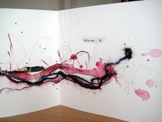 an open book with red and black ink splattered on the pages, sitting on top of a wooden table