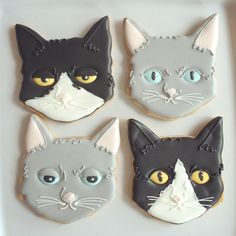 four decorated cookies in the shape of cats with yellow eyes and black, white, and gray colors