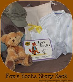 a teddy bear sitting next to a book and some clothes on a bed with the caption fox's socks story sack