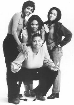 four women pose for a black and white photo in front of a white background with one woman leaning on the back of another