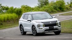 a white suv driving down a road next to lush green grass and trees in the background