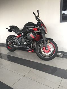 a red and black motorcycle parked in front of a white wall on a tiled floor