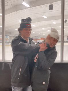 two men standing next to each other in front of an ice rink with their arms around one another